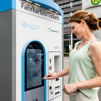 Eine Frau steht an einem Fahrkartenautomat.