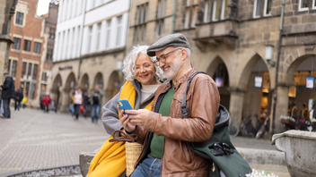 Älteres Ehepaar schauen auf ein Smartphone und sind in der Innenstadt unterwegs.
