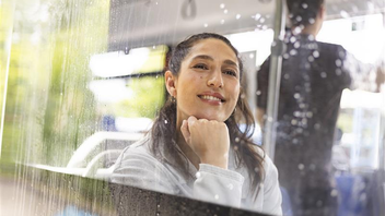 Eine Frau sitzt im Bus vor einer verregneten Bussscheibe und blickt sehnsüchtig nach draußen.