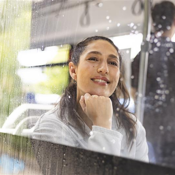 Eine Frau sitzt im Bus vor einer verregneten Bussscheibe und blickt sehnsüchtig nach draußen.