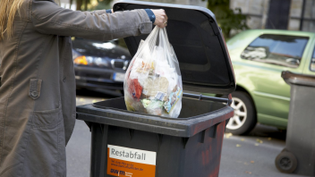 Müllsack wird in eine Mülltonne geworfen.