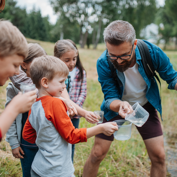 Ein Mann zeigt einer Gruppe von Kindern etwas in der Natur.